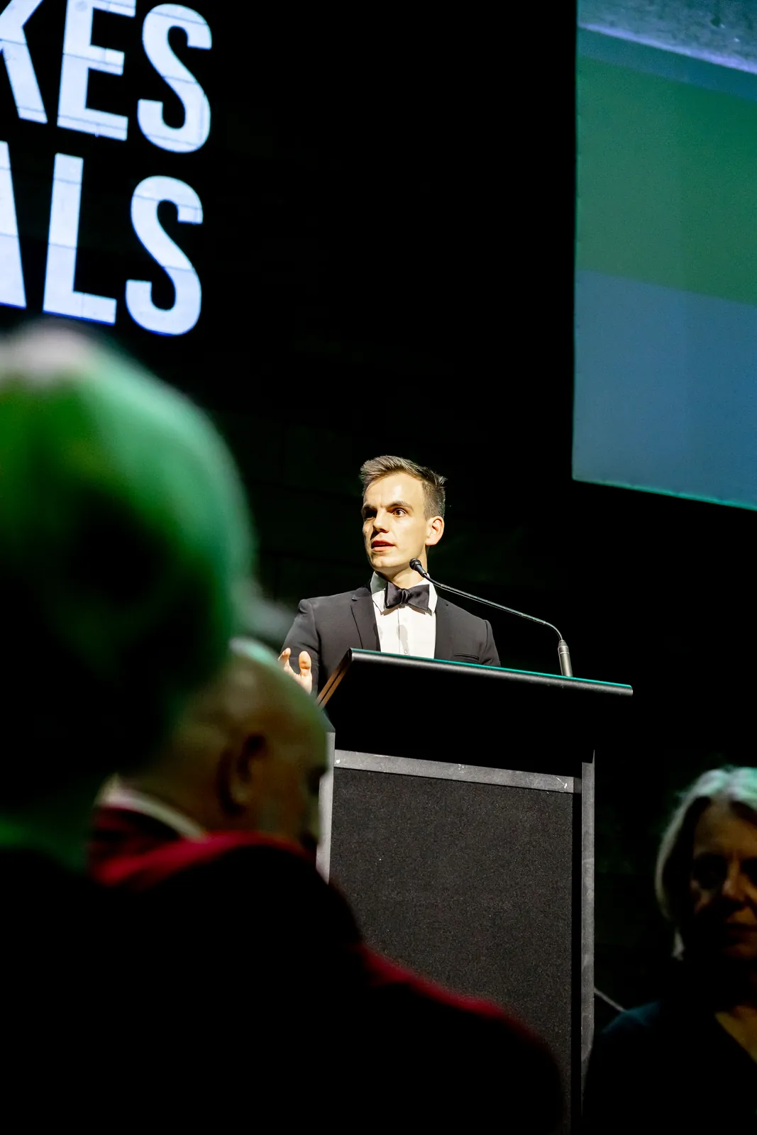 Alex speaking at the 2026 Feast To Feed gala, seen from the audience